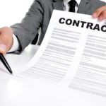 man wearing a suit sitting in a table showing a contract and where the signer must sign